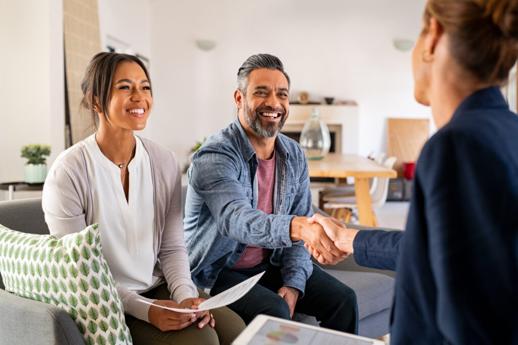 Mature indian man shaking hands with financial advisor at home. Happy smiling couple greeting broker with handshake at home. Multiethnic mid adult man and hispanic woman sealing a contract.