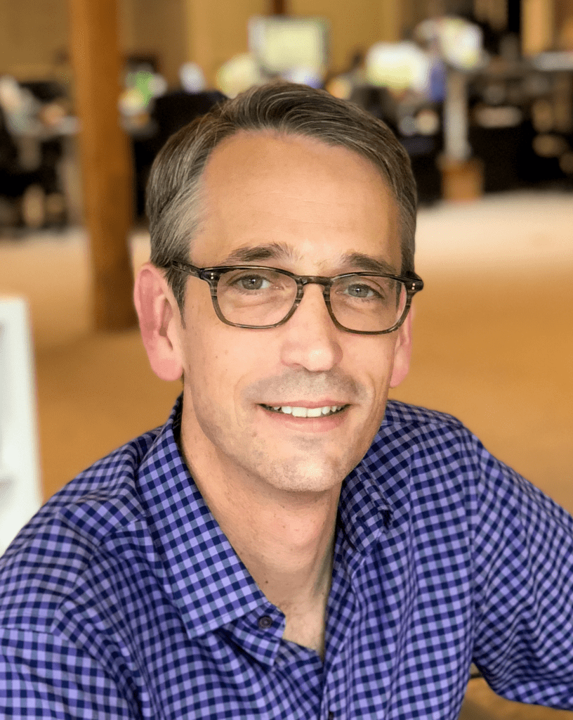 Executive Director of VertueLab, David Kenney, wearing a blue shirt and square glasses.